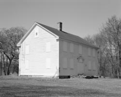 black and white image of a house with boarded up windows standing all alone in a field with trees in the background