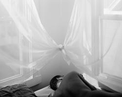 black and white image of a nude figure laying on a mattress in the corner of a room, flanked by curtained windows, curtains tied at the center corner