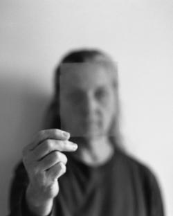 black and white photo of a person holding a piece of glass in front of their face with their hand, face out of focus