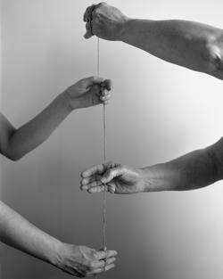 black and white photo of a set of arms face another as each pulls a piece of twine taut