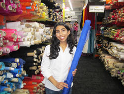 Nura Dhar holds a spool of blue fabric in a room filled with fabric samples