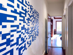 a blue and white QR code runs along a white hallway wall toward an open door leading toward a sunlit window