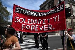 People march through the street holding a large banner that reads "Student Worker Solidarity! Forever."