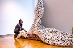 A graduate student at RISD is installing a large woven artwork in a gallery space.