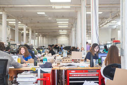 several rows of students sit at workstations inside a studio workshop