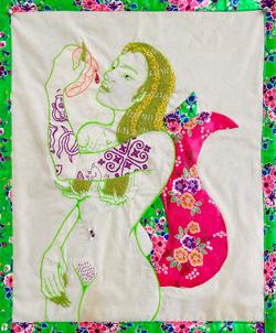 a white fabric embroidery featuring the outline of a nude woman eating a heart
