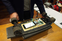 a person overlooks a skateboard turned bottom up, outfitted with a phone-sized touchscreen and circuitboard