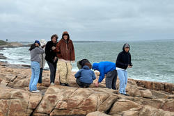 Students stand on large rocks by the ocean