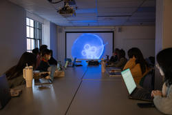 Students watch a video in a dark room on a projector screen showing a blue jellyfish