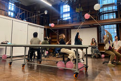 A group of students play a game featuring pink balloons on sticks
