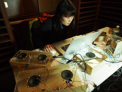 a student sits behind a laptop, surrounded by several gold metallic boxes outfitted with wired audio speakers