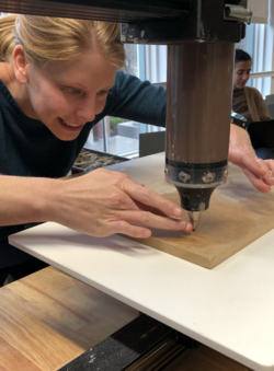 a student guides a 3d printer filled with brown clay along a work surface