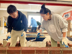 two students working in the studio with bricks and mortar