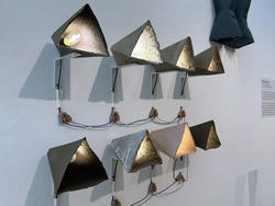 eight triangular clay lamps mounted on a wall in two rows of four, several illuminated