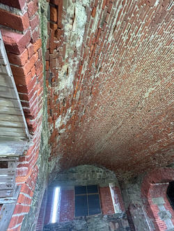 an overhead view of a curved ceiling made of worn brick, supported by a similarly worn-brick entryway