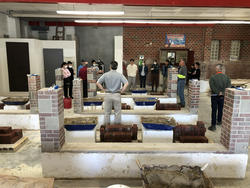 students gather around craftsperson in workspace filled with several neat stacks of brick