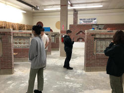 several students observe and photograph sample brick assemblages in a warehouse space