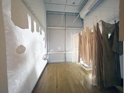 white, light brown, and dark brown fabric sheets hanging from ceiling to floor along a gallery corridor