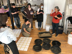several students gather around an artist discussing work, with six dark clay vessels in the foreground