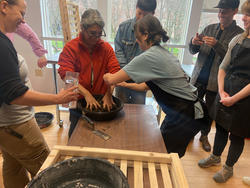 students and visiting artist shape a clay vessel together inside a studio space