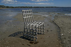 a beach chair made with organic materials sits on a beach, with coastal waters in the background