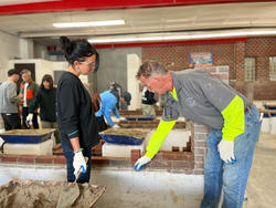 a student and a brick tradesperson discuss a bricklaying project inside a workroom