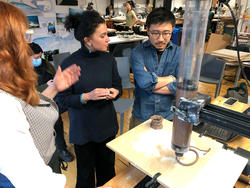 three people gather around a 3d printer extruding clay