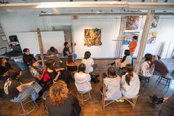 approximately 15 students gather in a studio space for a critique of student work