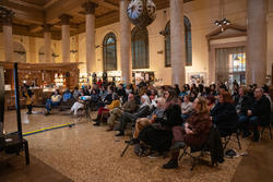 A crowd fills a room for a presentation in a library