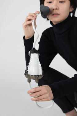 A person in black holds a white and black metal piece up to their face.