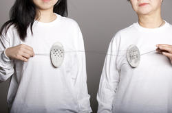 Two people hold two metal oval artworks connected by thin strings between the two of them.
