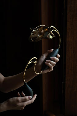 A pair of hands are holding up a winding warm-toned metalwork joined together with black connecting pieces.