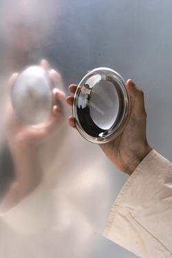 A hand in a white shirt is holding up a spherical artwork in front of a frosted mirror.