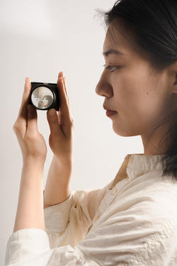 A student in a white shirt is holding a jewelry piece featuring a camera display.