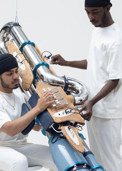 Two students are holding a large musical metal and wooden artwork.