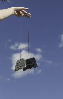 A person is dangling two metal artworks from a thread.