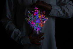 A person in a white shirts holds a multicolored artwork in the shape of an ornate heart.