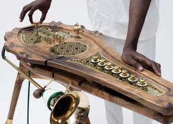 A person in white is interacting with a wooden and metal musical artwork.
