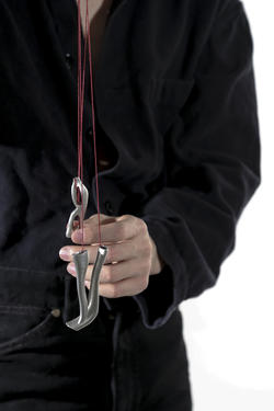 A person wearing black is dangling two small metalworks from red string.