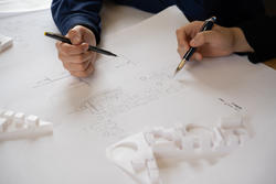 two hands holding pens work on an architectural drawing