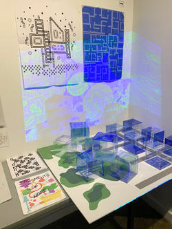 Graphic Design student work by Joyce Kim of a 3d cubic display projecting images onto a wall with posters.