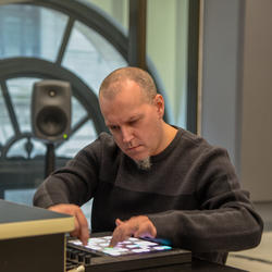 Shawn Greenlee operates a digital sound tool inside a room with speakers and a large window in the background