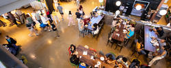 a bird's-eye view of people sitting at several long tables inside a dining hall