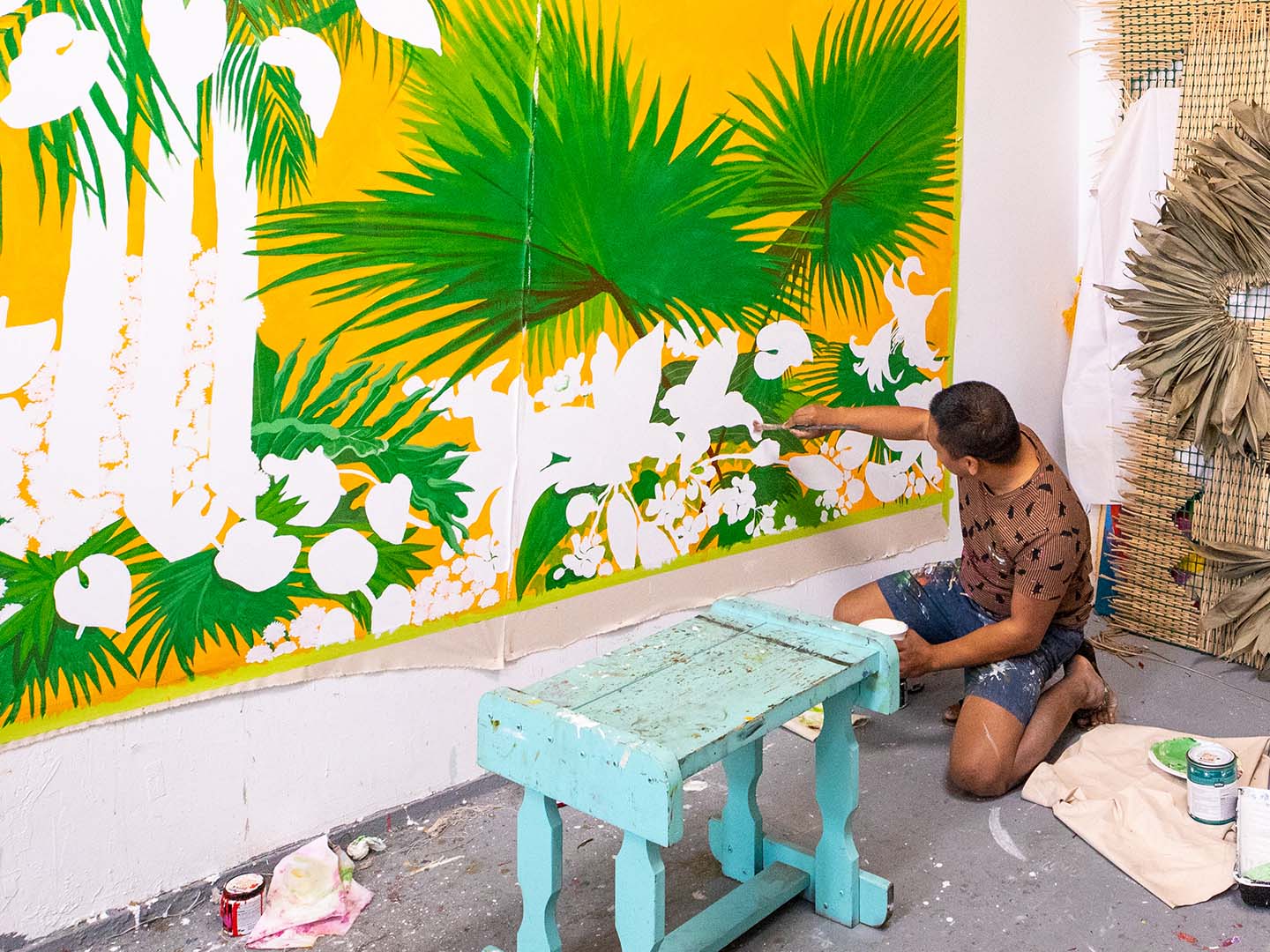 Student crouching and working on a large yellow and green painting in a painting studio.