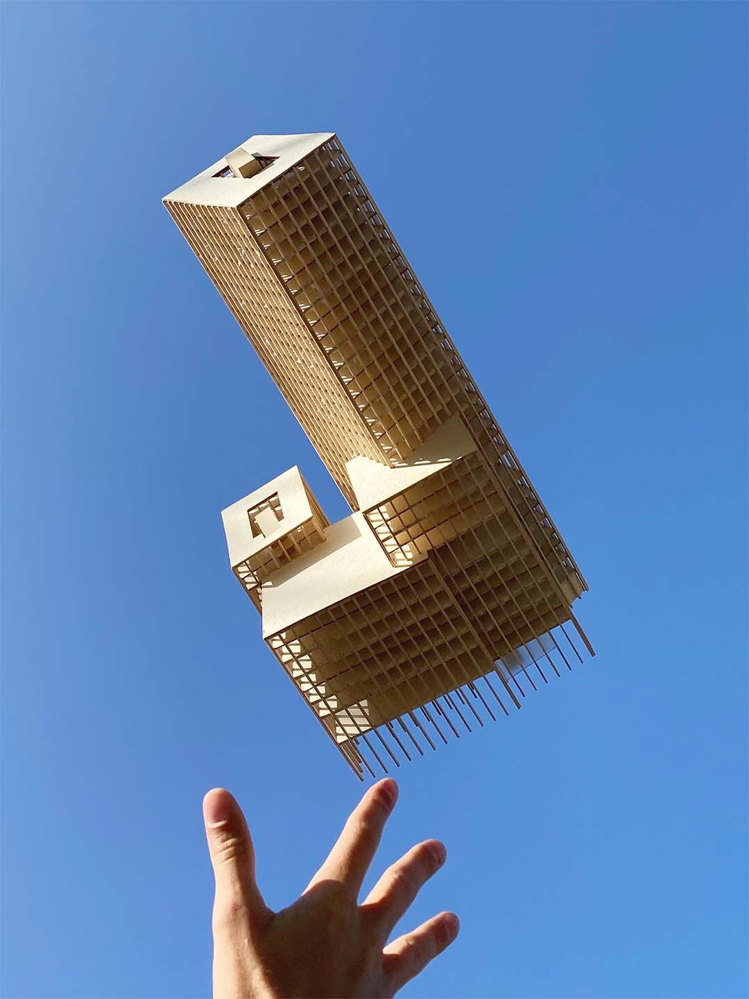 Wooden architectural model being thrown into sky by one hand.