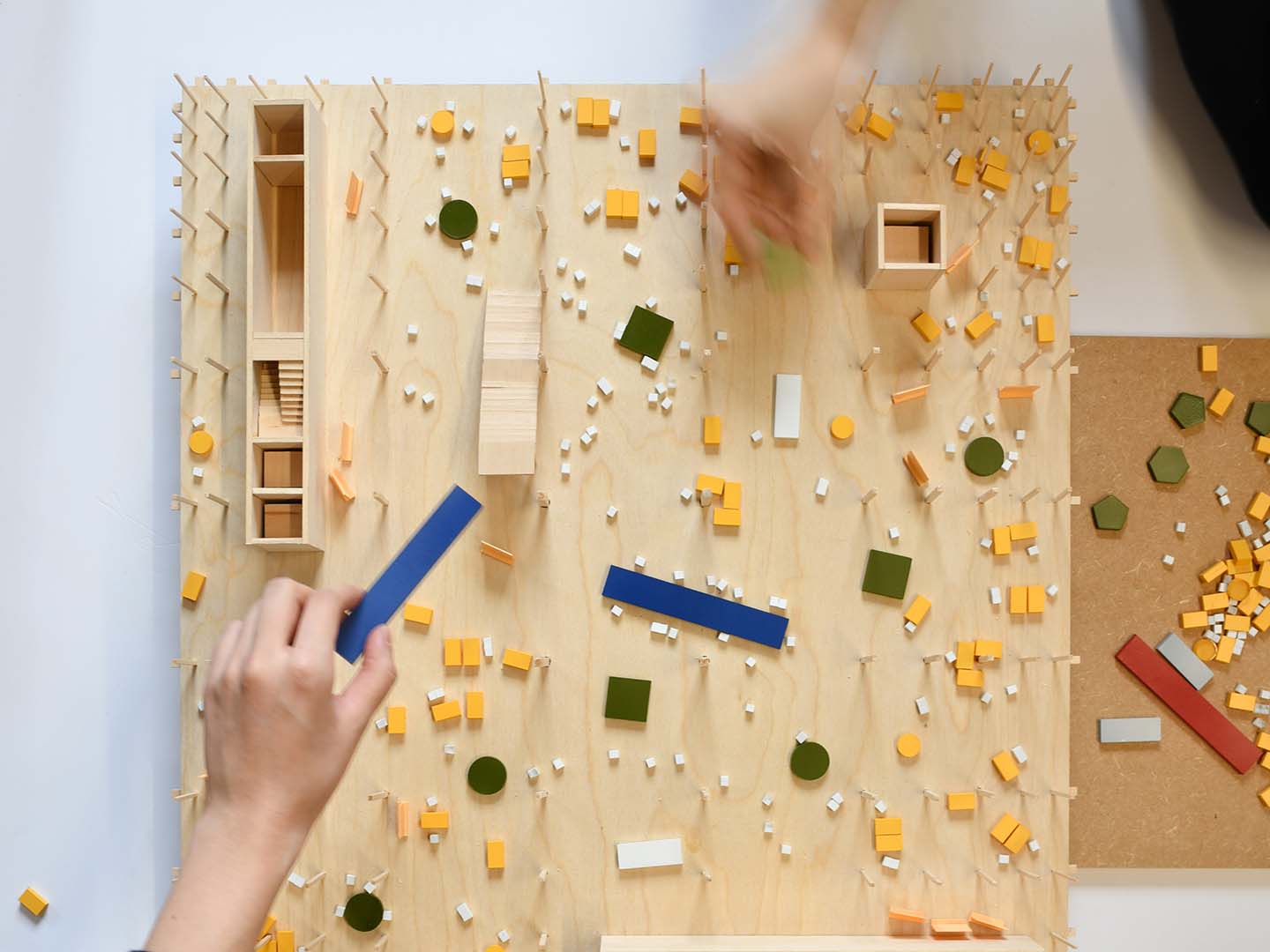 Overhead shot of two hands placing blocks on a graphic wooden and painted architectural model.